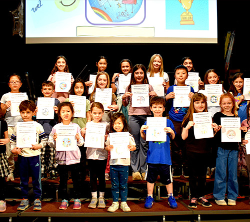 Group of children on stage holding certificates during a school recognition event.