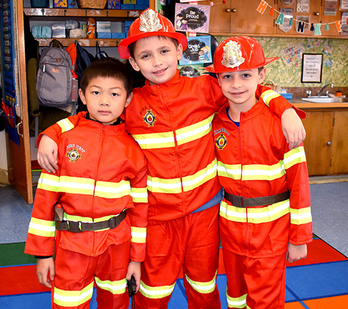 Person in a superhero lizard costume walking down an aisle, high-fiving smiling children.