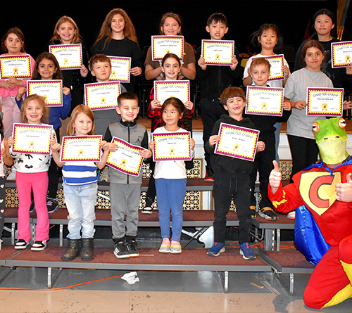 Group of children holding Charter Champs certificates with a costumed character posing beside them.