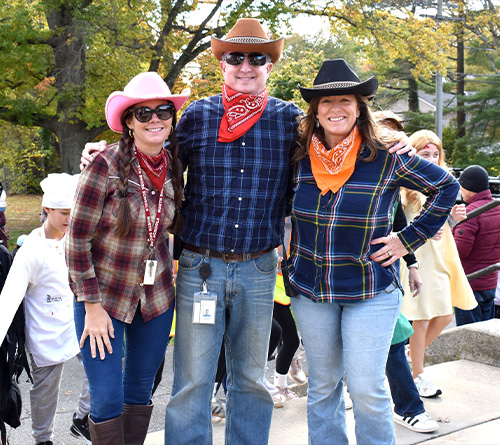 Three people dressed in cowboy and cowgirl costumes smiling outdoors during a Halloween event.