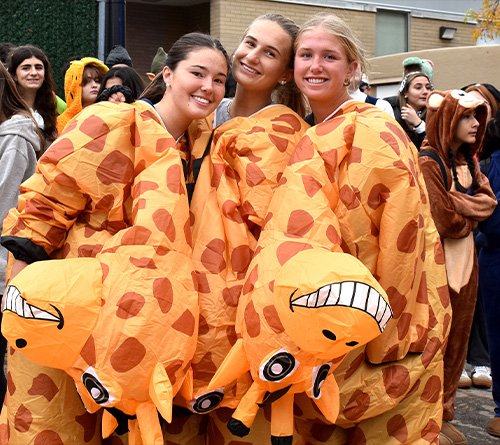 Three people wearing matching inflatable giraffe costumes smiling during a Halloween event.