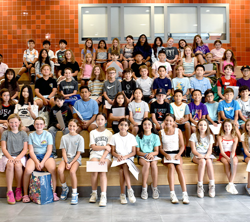 Group of students sitting and standing on tiered steps inside a school building.