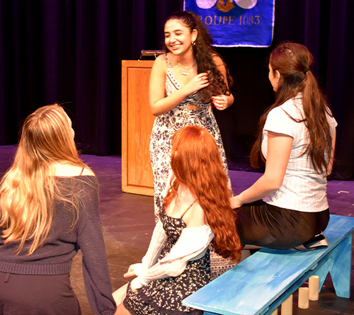 A group of students standing on stage holding certificates, posing for a photo during an honor society event with a blue and gold banner in the background.