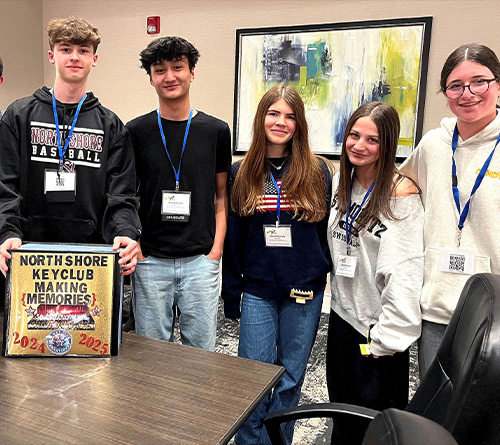 Key Club members stand together holding a decorated poster during a school event.
