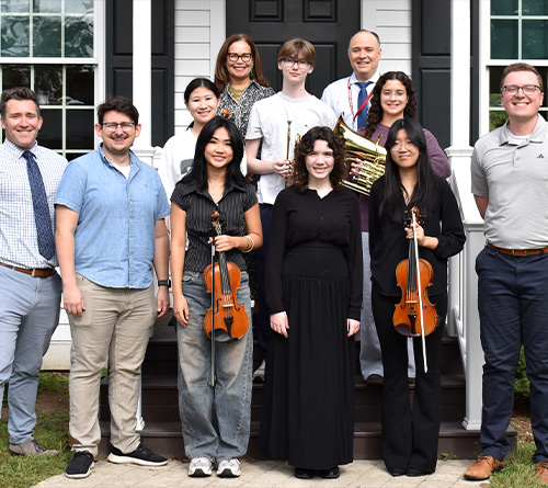 Group photo of students with instruments and teachers outside a building.