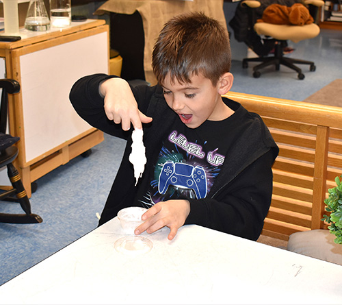 Young child excitedly playing with slime at a classroom table.