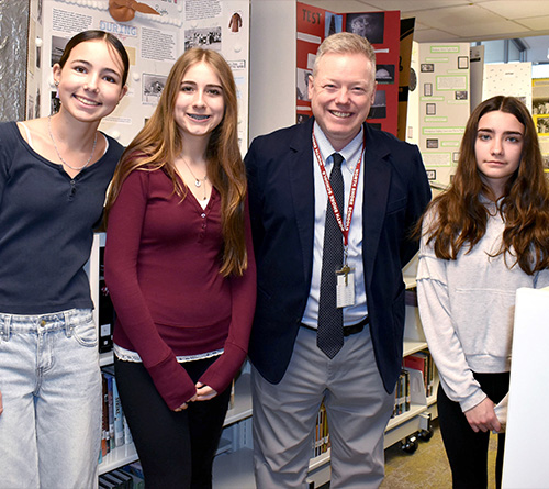 Teacher posing with three students at a school history project exhibit.
