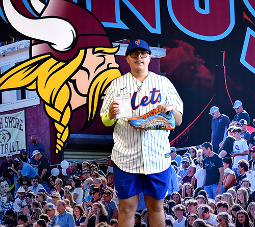 Student holding a baseball lineup card and custom cleat at a North Shore Vikings event.