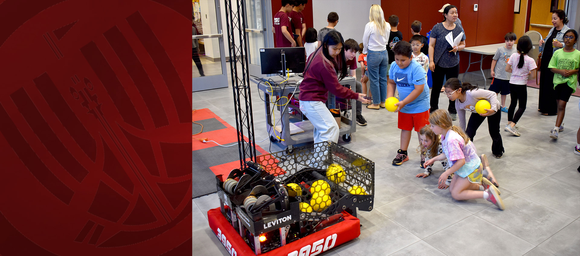 Children participate in a robotics activity, placing yellow balls into a robot game field while others watch.